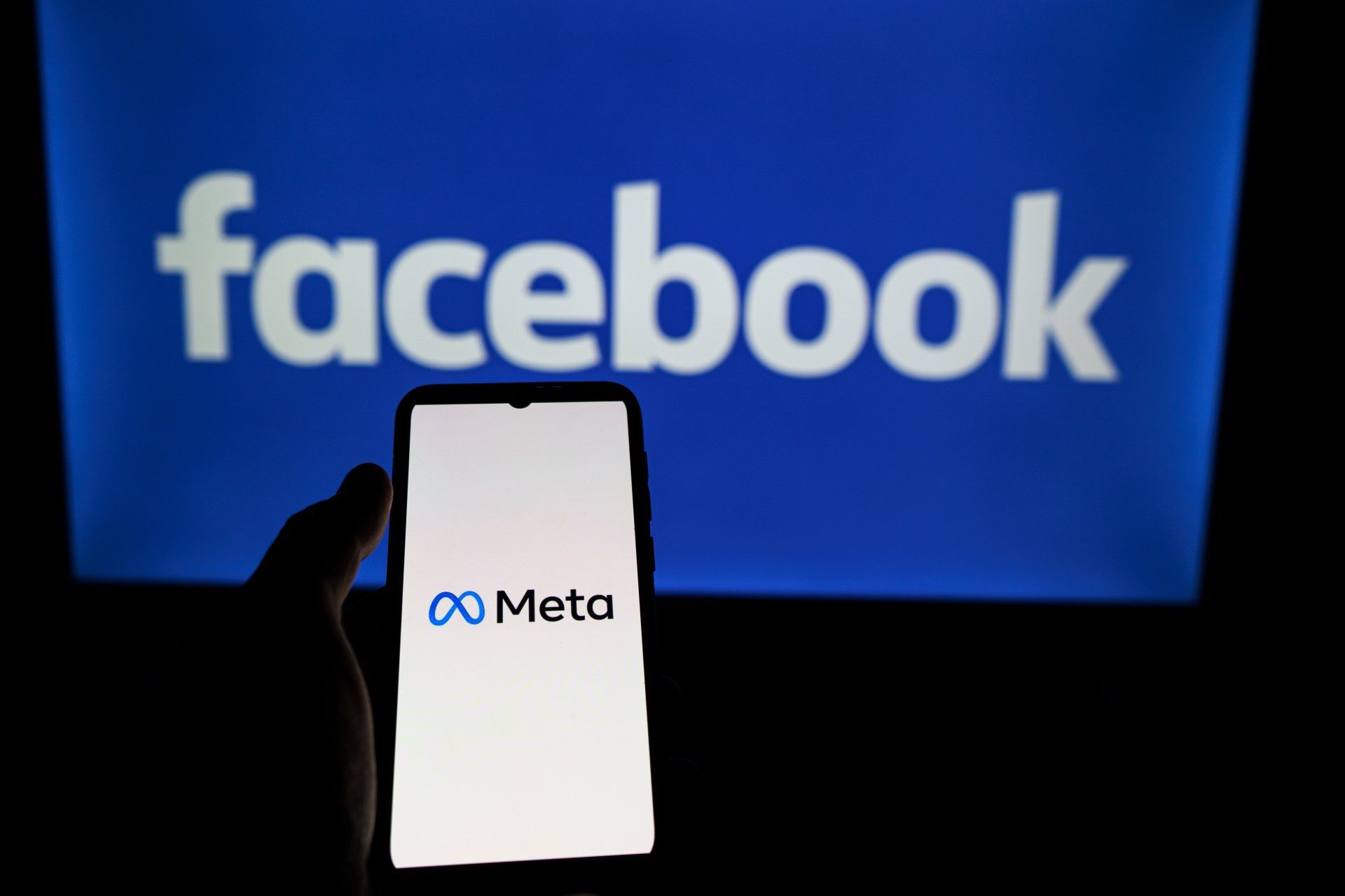 A person is holding a cell phone in front of a facebook logo.