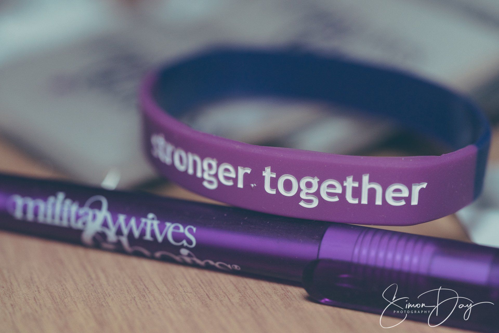 A purple bracelet that says stronger together is next to a purple pen
