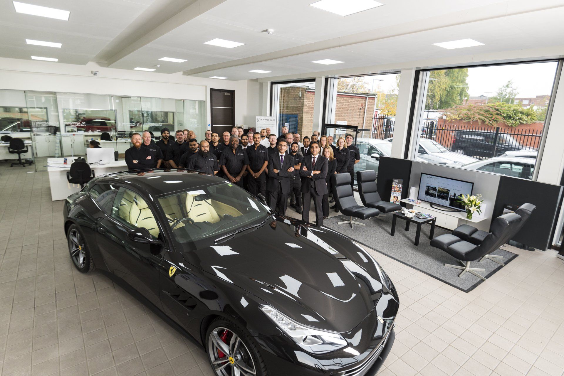 A group of people standing around a black car in a showroom.