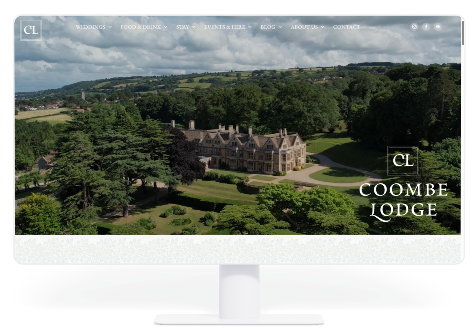 Desktop computer screen showing the Coombe Lodge website homepage featuring an aerial view of the historic estate.