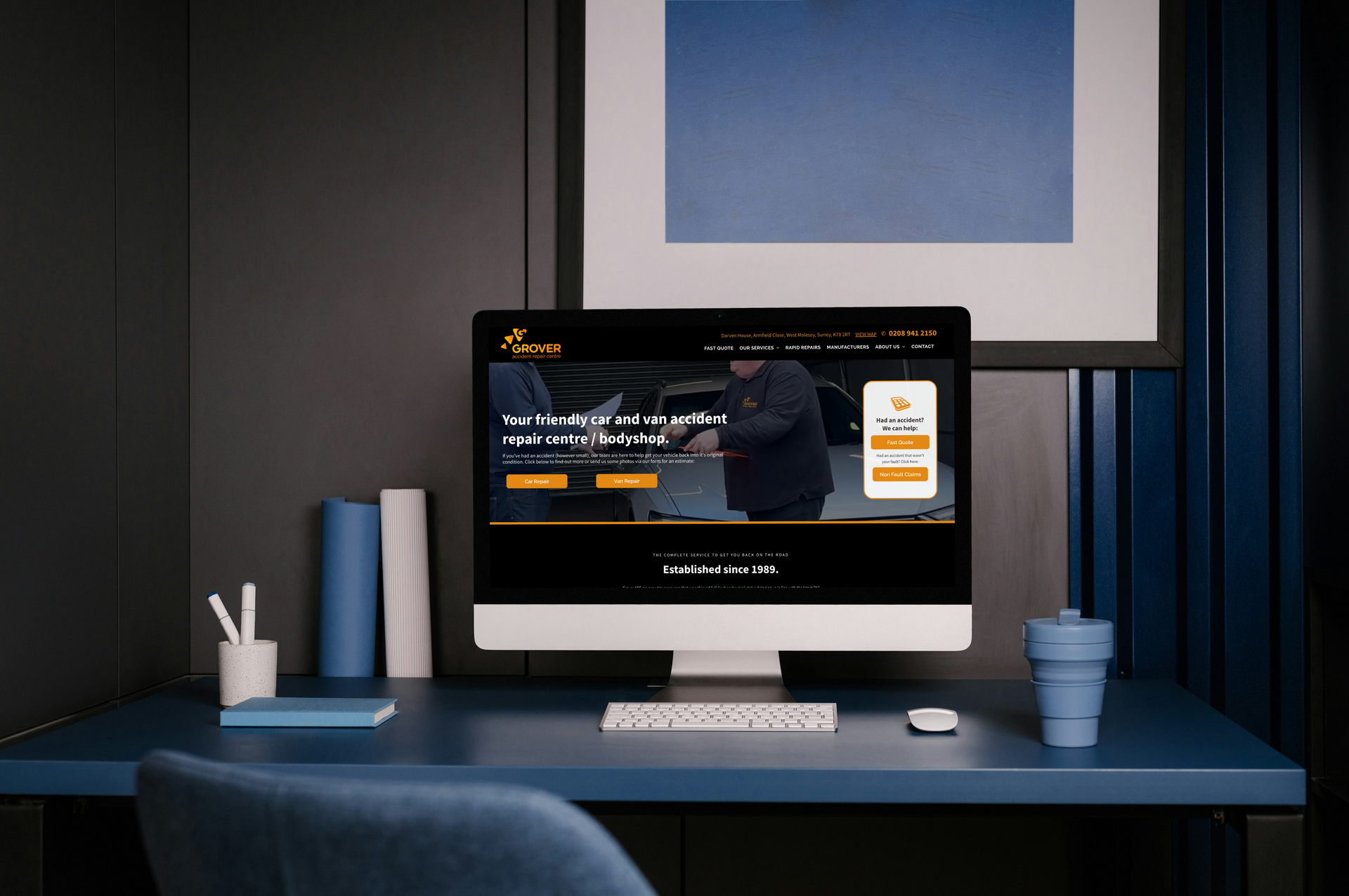 Computer displaying a website with a man in an auto shop. Desk with books, cup, and keyboard.