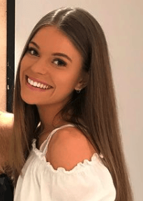 A woman with long hair is smiling and wearing a white off the shoulder top.