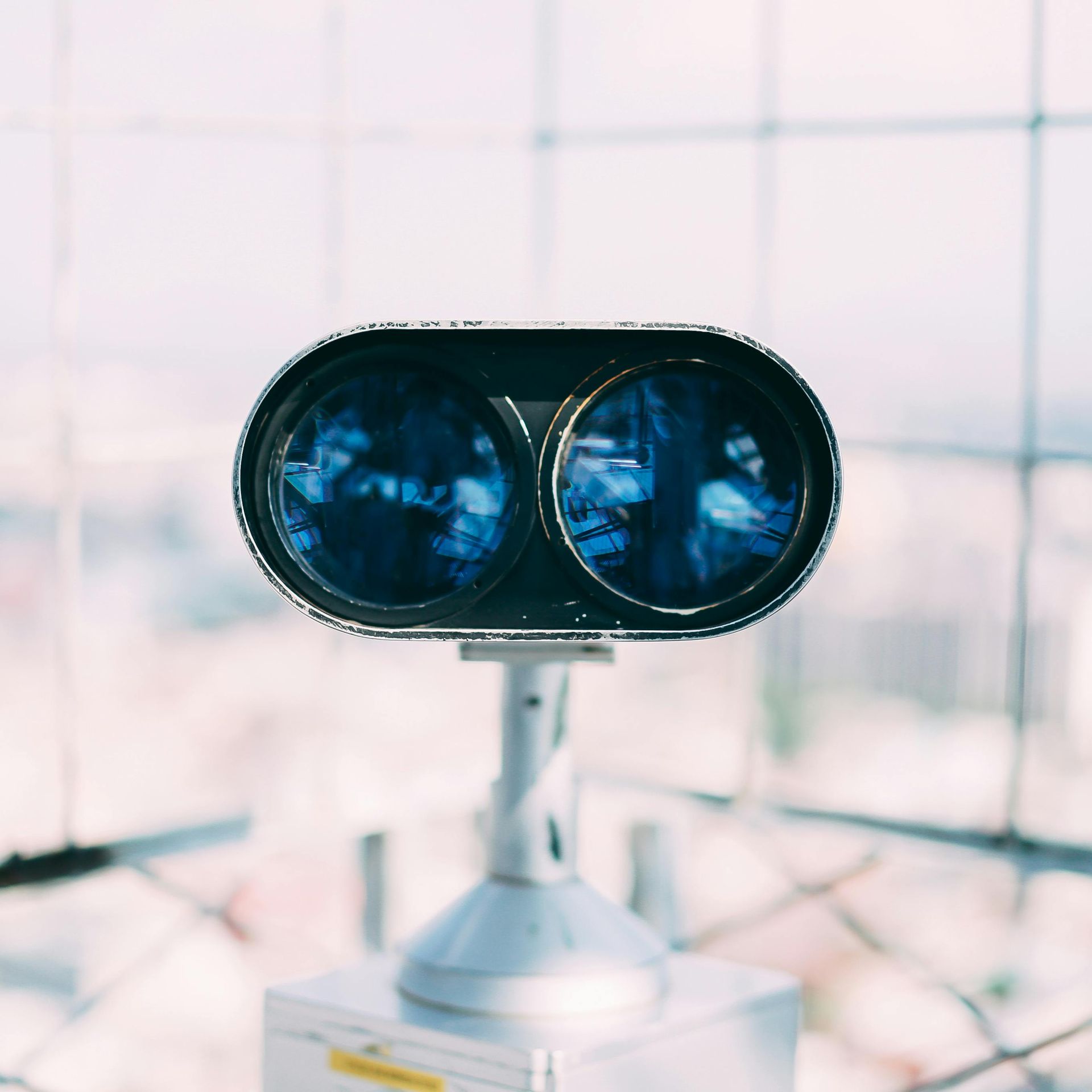 A stationary coin-operated tower viewer with circular lenses, set against a bright, out-of-focus background.