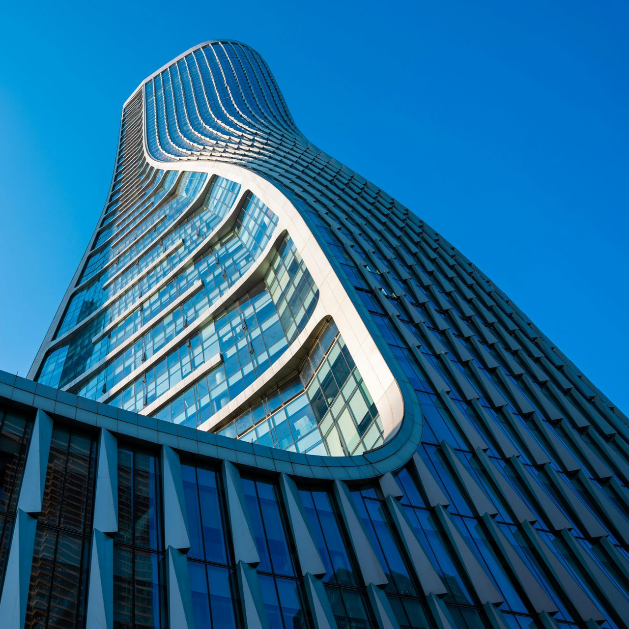 A tall, modern skyscraper with a distinctive curved facade and blue glass windows rising against a clear blue sky.