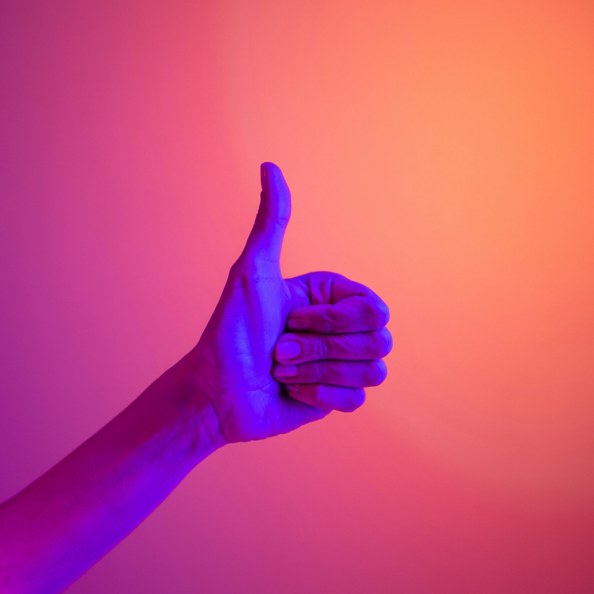 A hand makes a thumbs-up gesture against a vibrant, purple-to-orange gradient background.