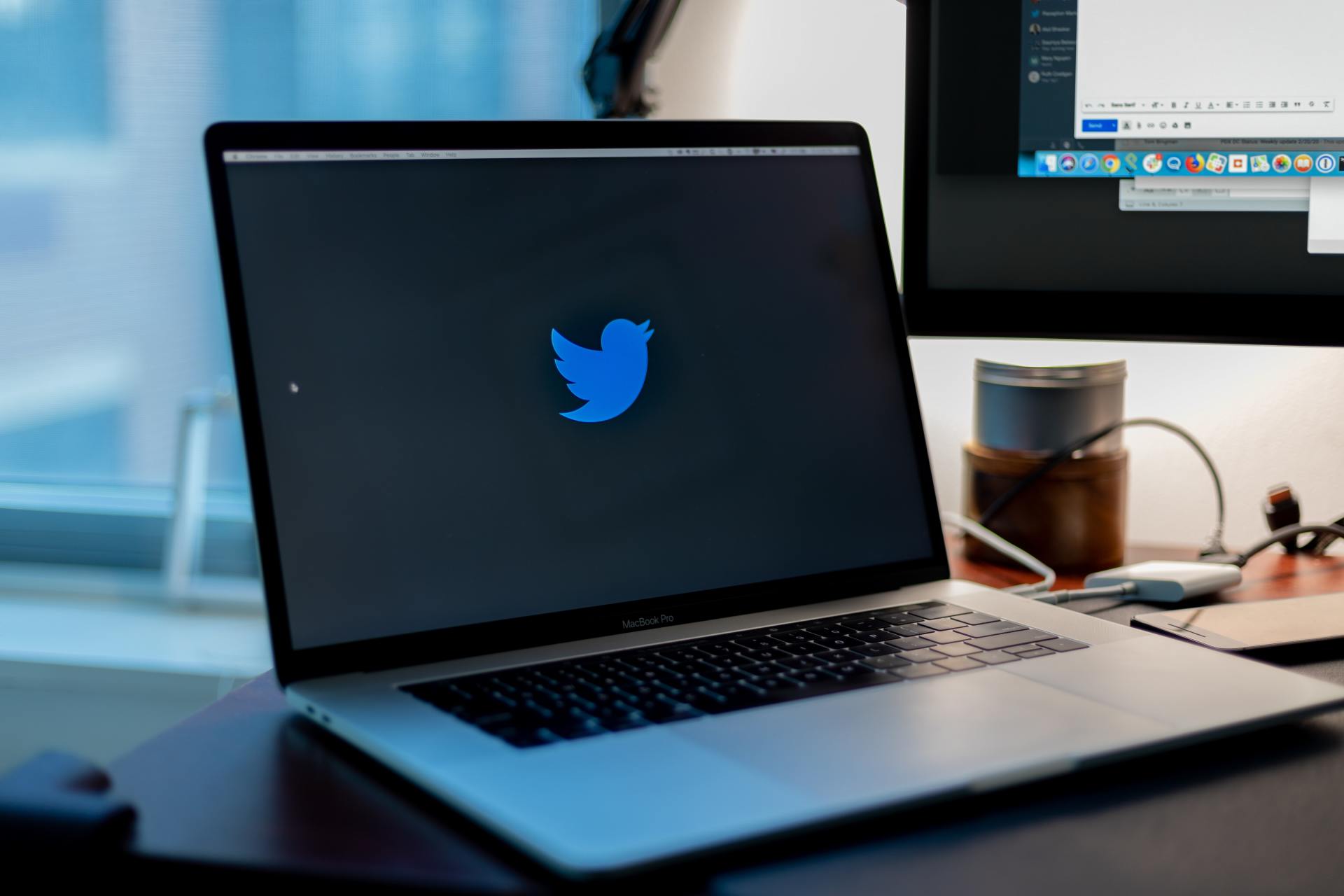 A laptop with a twitter logo on the screen is open on a desk.