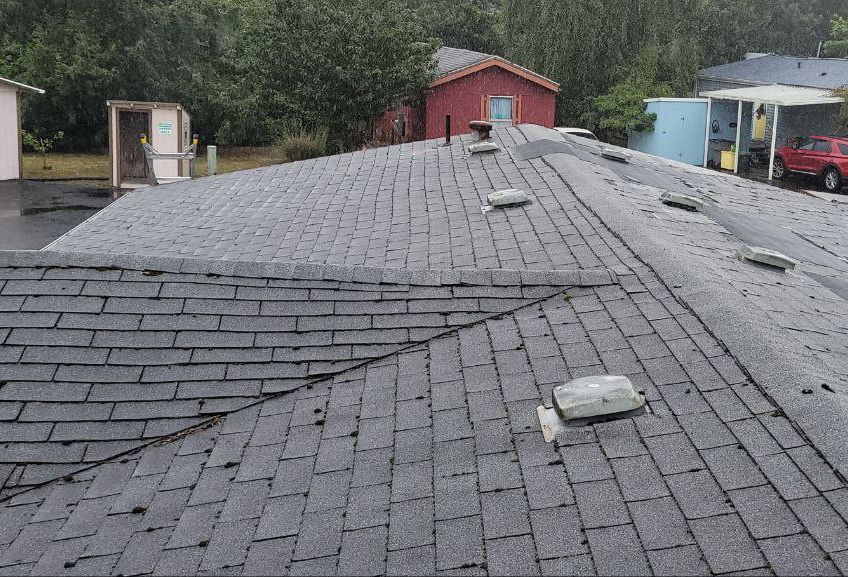 A roof with a lot of shingles on it and a red house in the background.