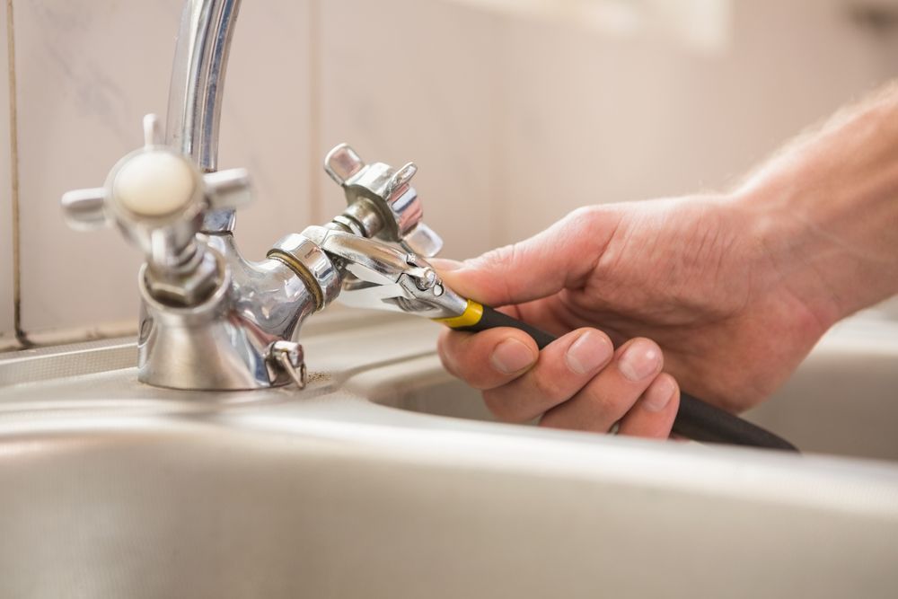 Person Using a Wrench to Repair a Faucet in a Kitchen Sink — Stewys in Tweed Heads, NSW