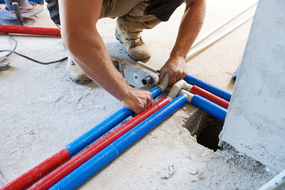 Plumber Installing Red and Blue Pex Pipes, Using a Tool, on a Concrete Floor — Stewys in Casuarina, NSW