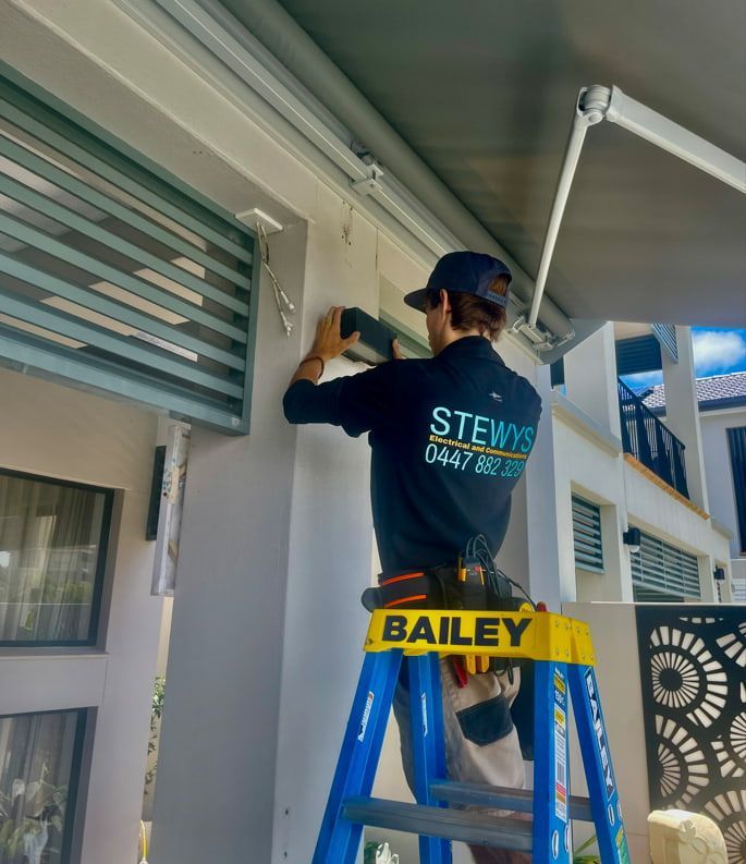 A Man is Standing on a Bailey Ladder Working on an Awning — Stewys Electrical and Communications In Casuarina, NSW