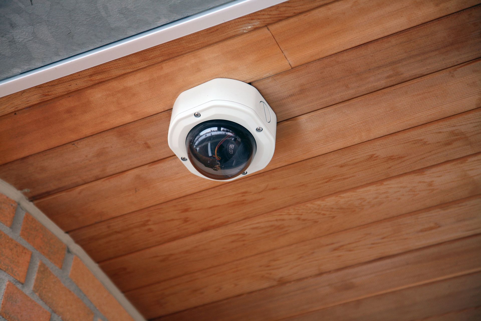 White Security Camera Mounted on a Wood Plank Ceiling, Near a Brick Wall — Stewys Electrical and Communications In Tweed Heads, NSW