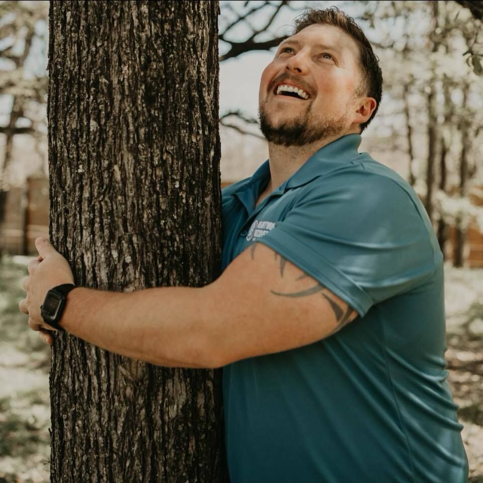 A man in a blue shirt is hugging a tree