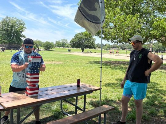 Two men are playing a game at a picnic table in a park.
