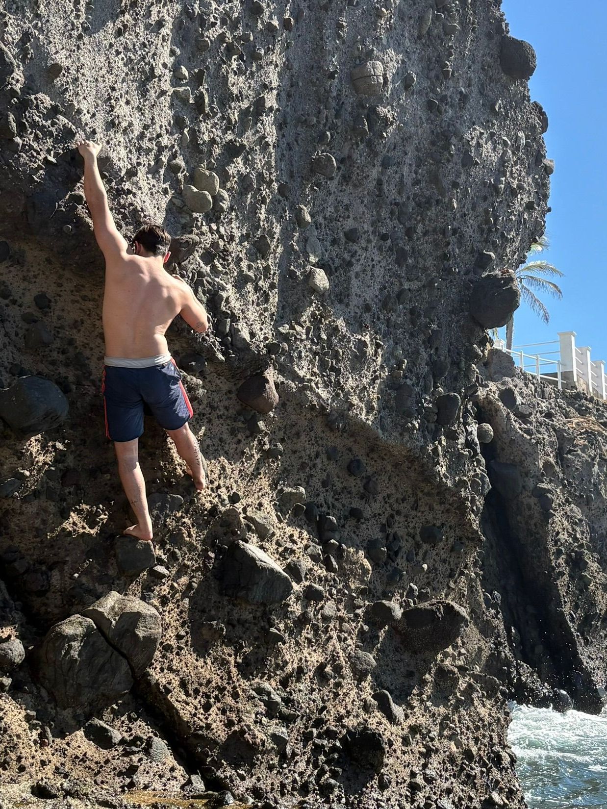 A man is climbing up a rocky cliff near the ocean