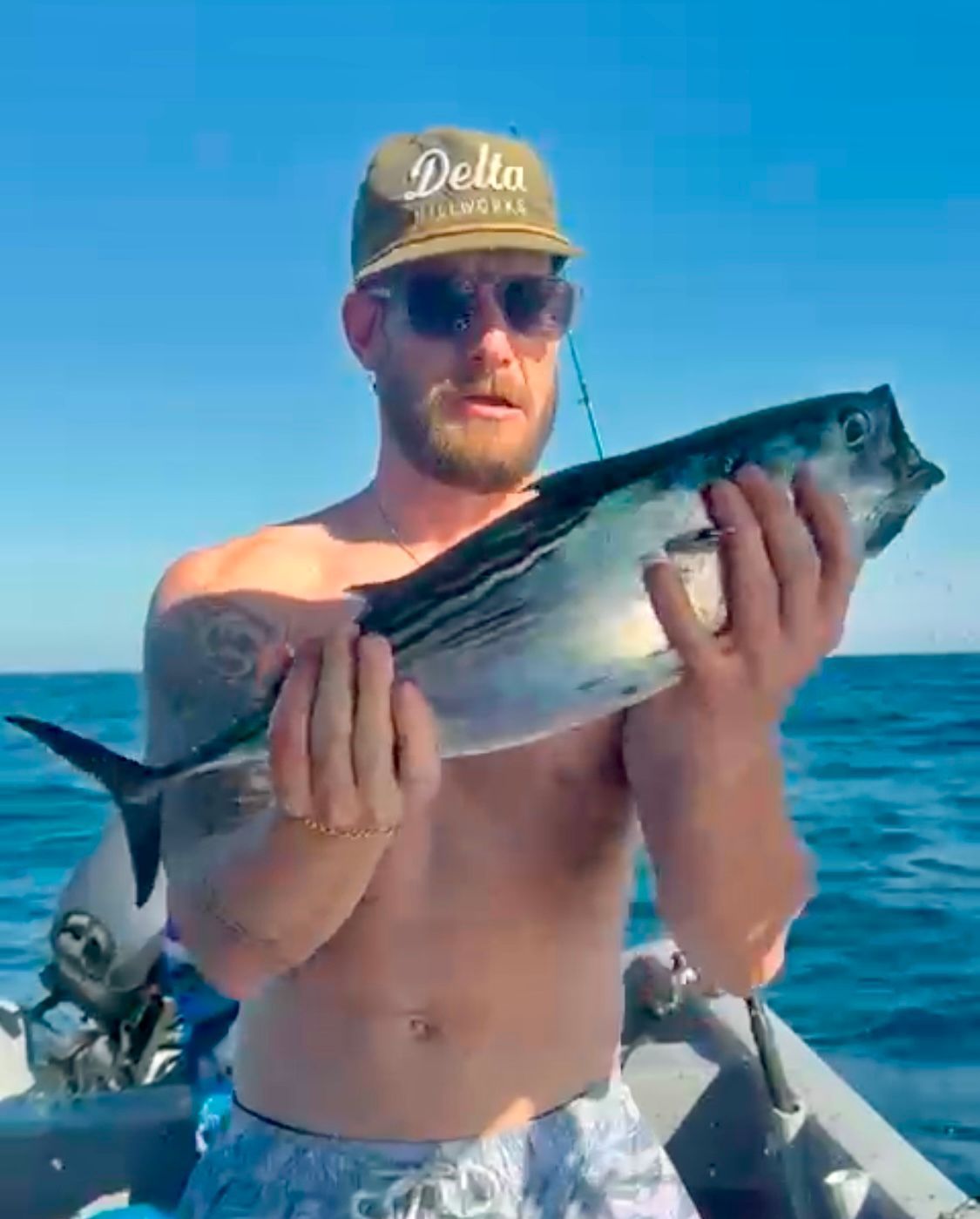 A shirtless man is holding a fish in his hands on a boat.