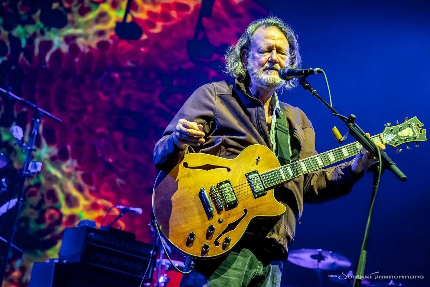 A man in a cowboy hat is standing in front of a group of people in a park.