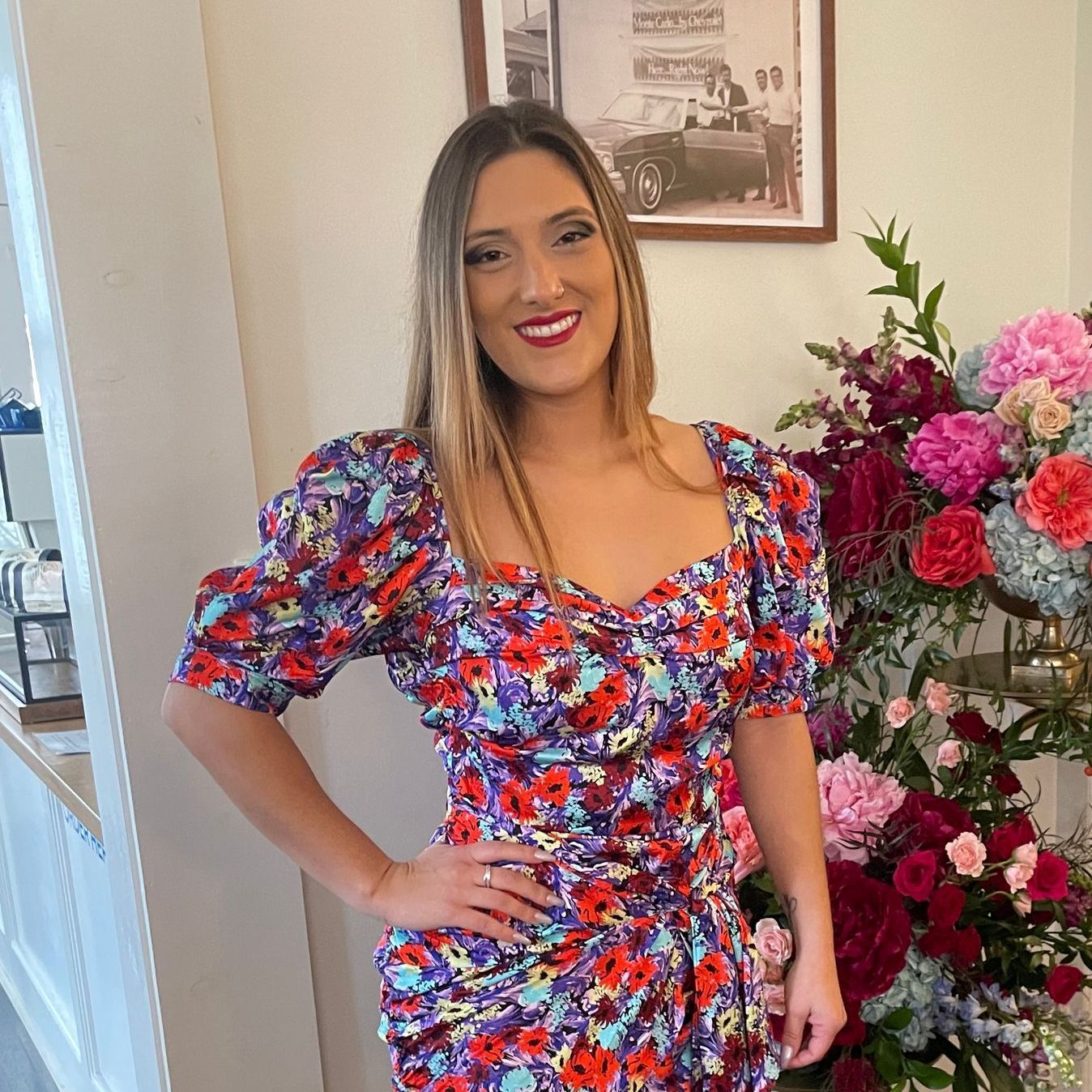 A woman in a floral dress is standing in front of a vase of flowers.