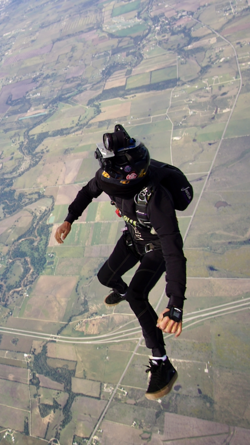 A man in a black suit is jumping in the air.