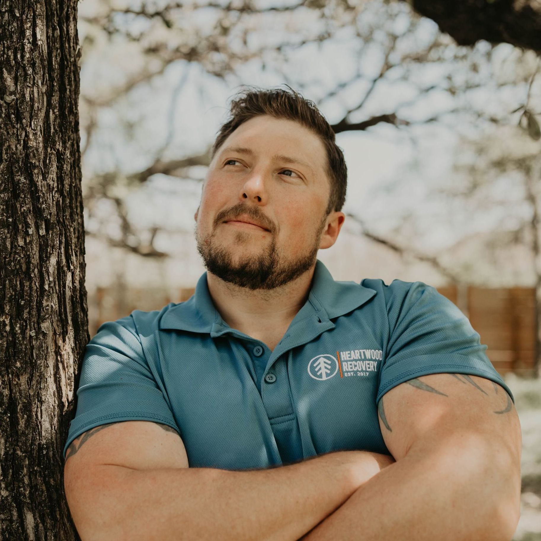 A man leaning against a tree with his arms crossed
