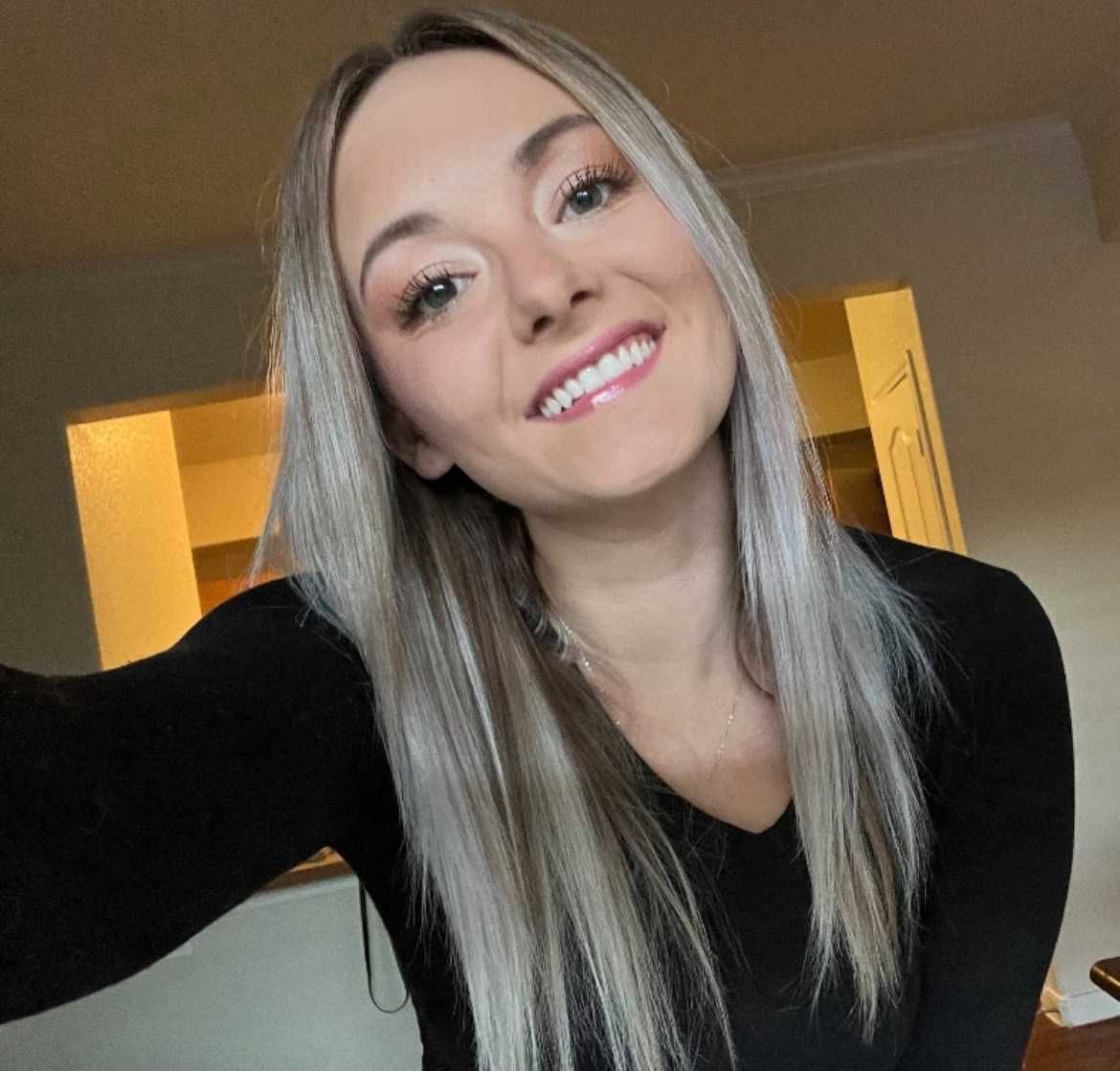 A woman in a black shirt is smiling and taking a selfie.