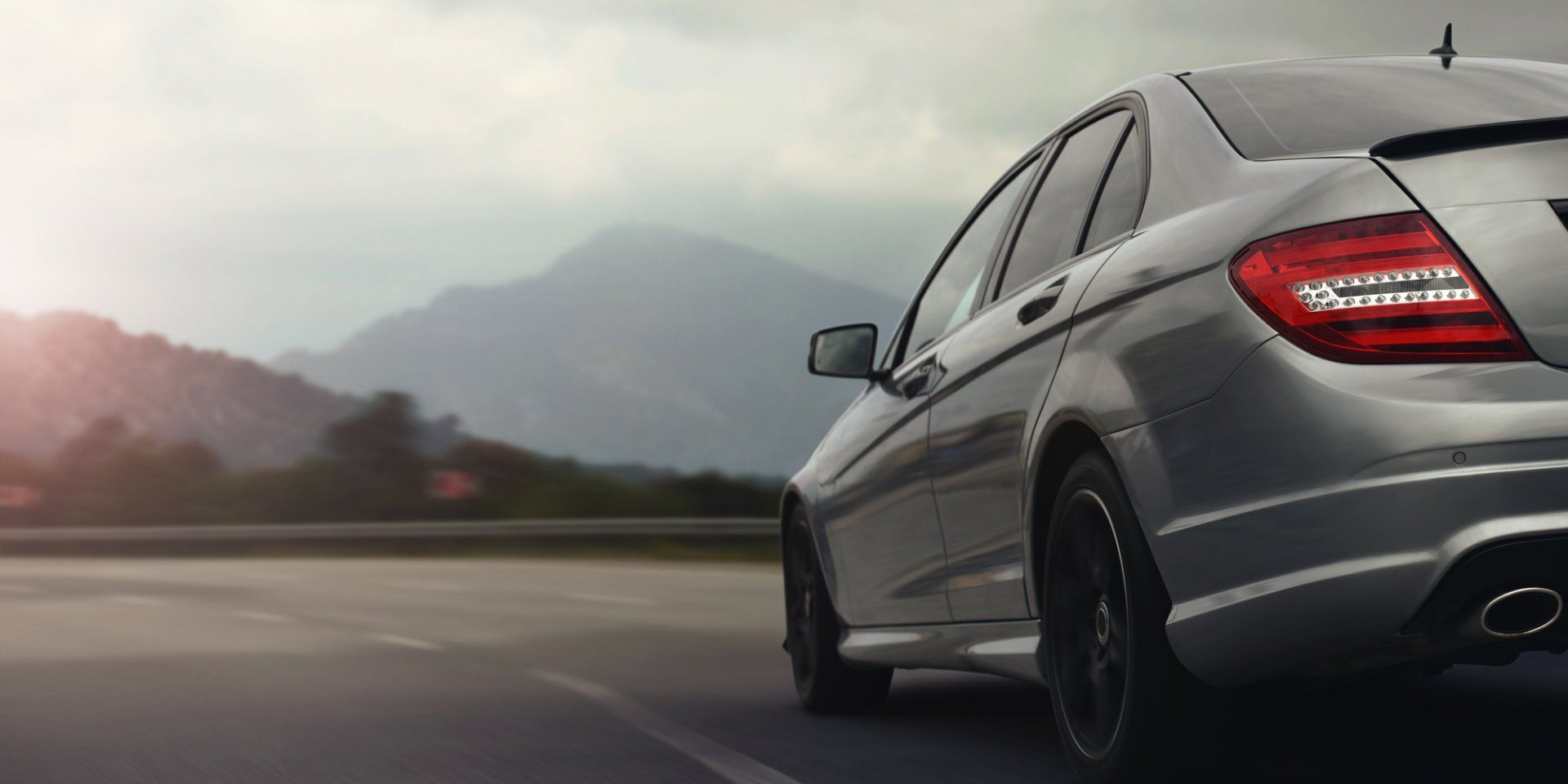 Silver sedan driving on a road, with a mountain range in the background under a cloudy sky. | Nevarez Body Shop