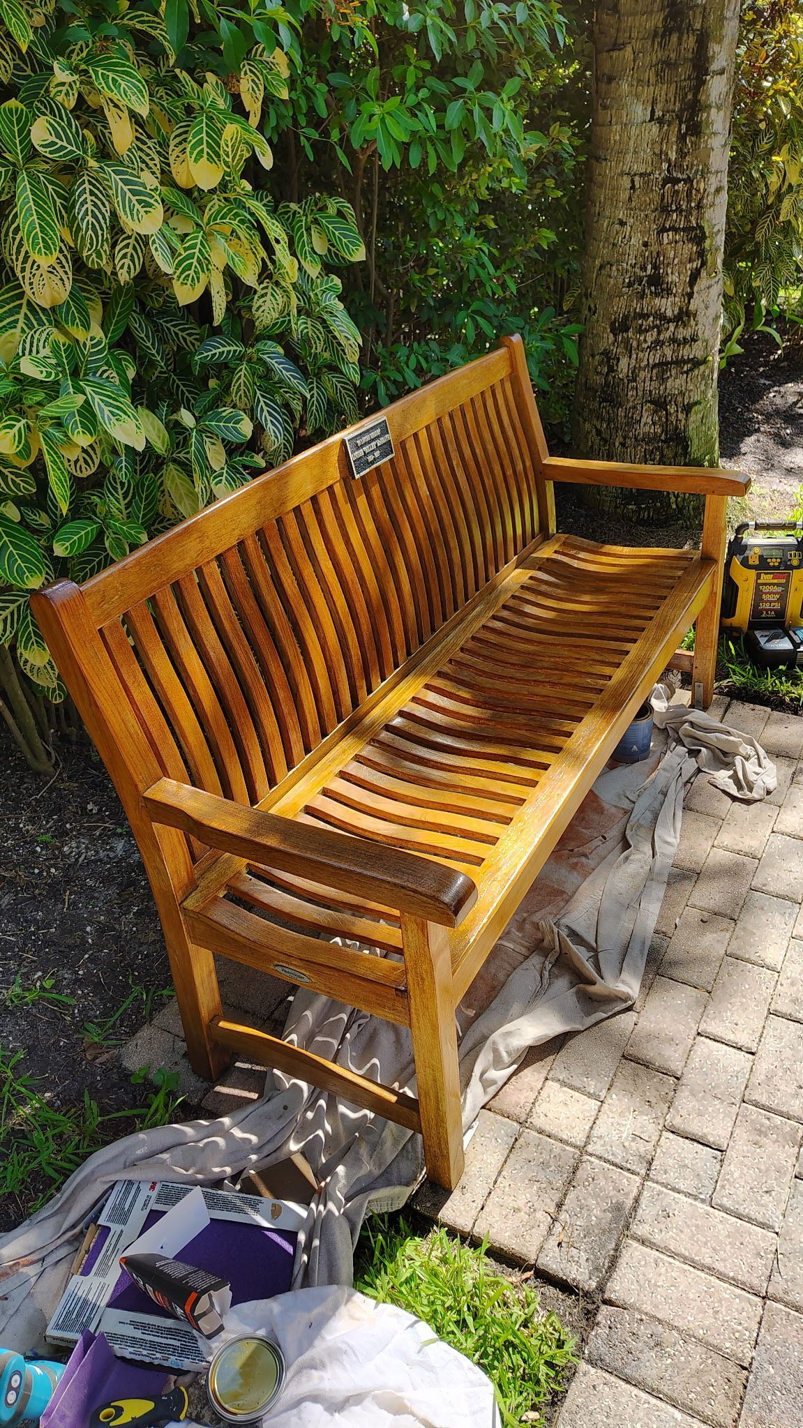 A wooden bench is sitting on a brick sidewalk next to a tree.