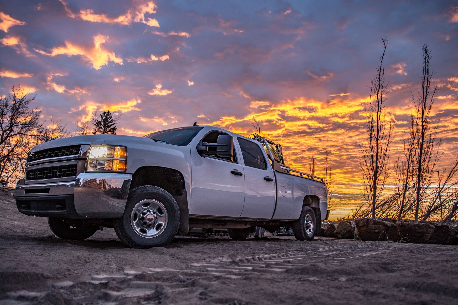 Silver pickup truck on a dirt road, with a sunset in the background.