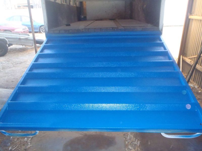 Blue ramp extending from a truck bed, featuring horizontal ridges and handles.