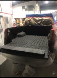 Truck bed, black textured coating, in a workshop setting. Protective coverings are in place.