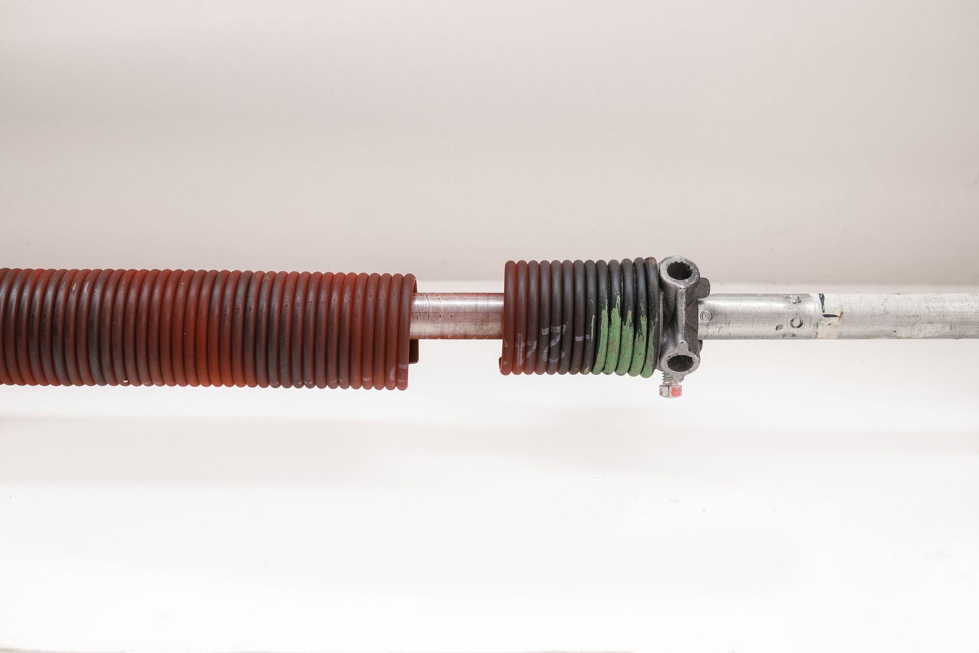 A close-up of a rusty garage door spring on a white surface.