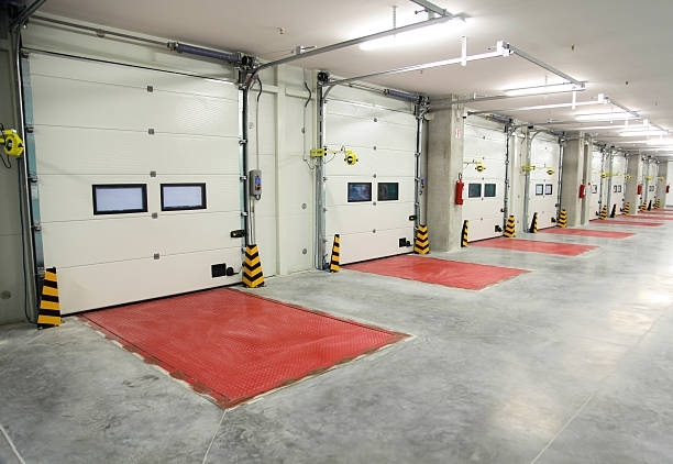 A row of white garage doors with red mats in a warehouse.