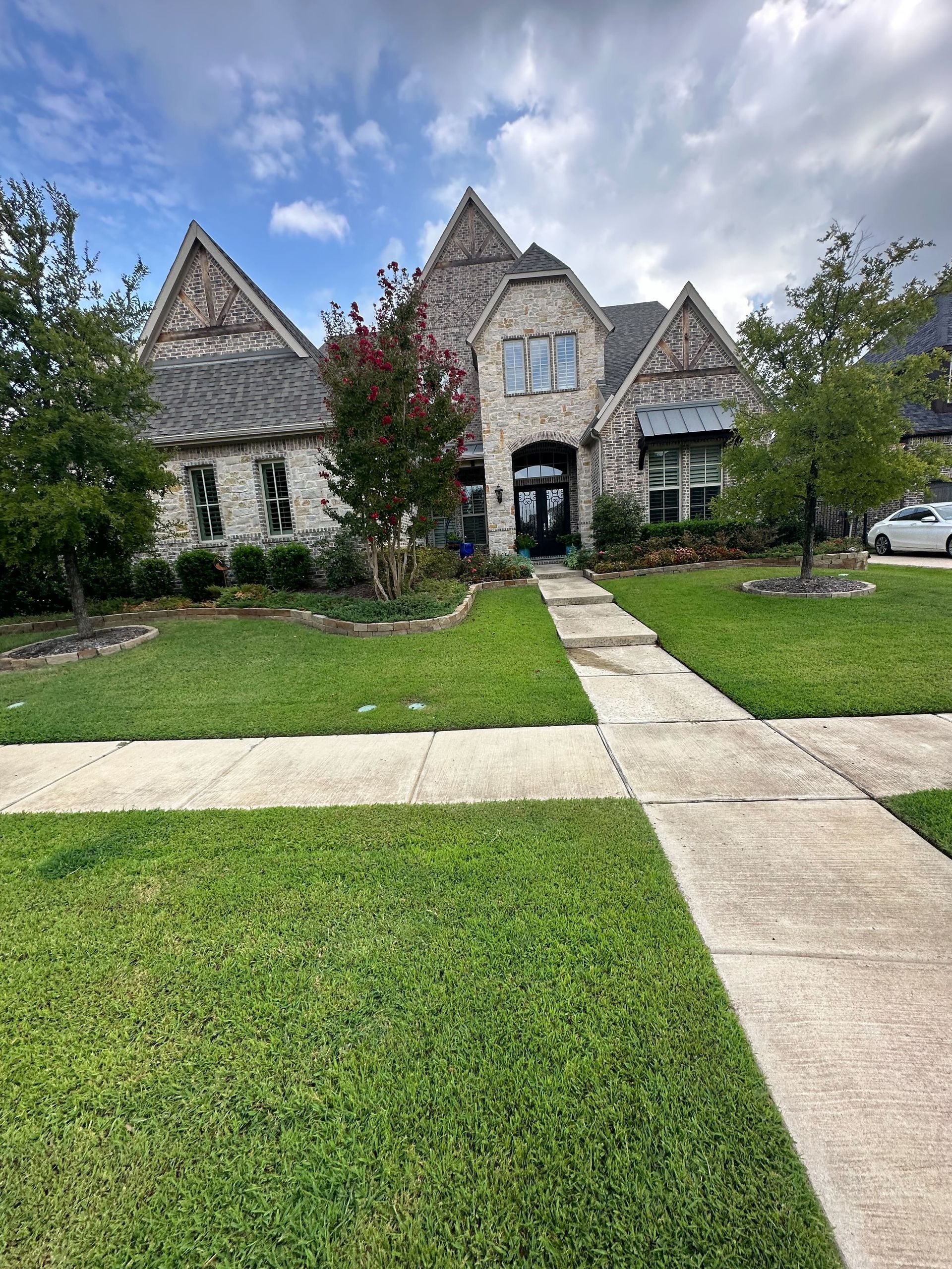 A large brick house with a lush green lawn and a sidewalk in front of it.