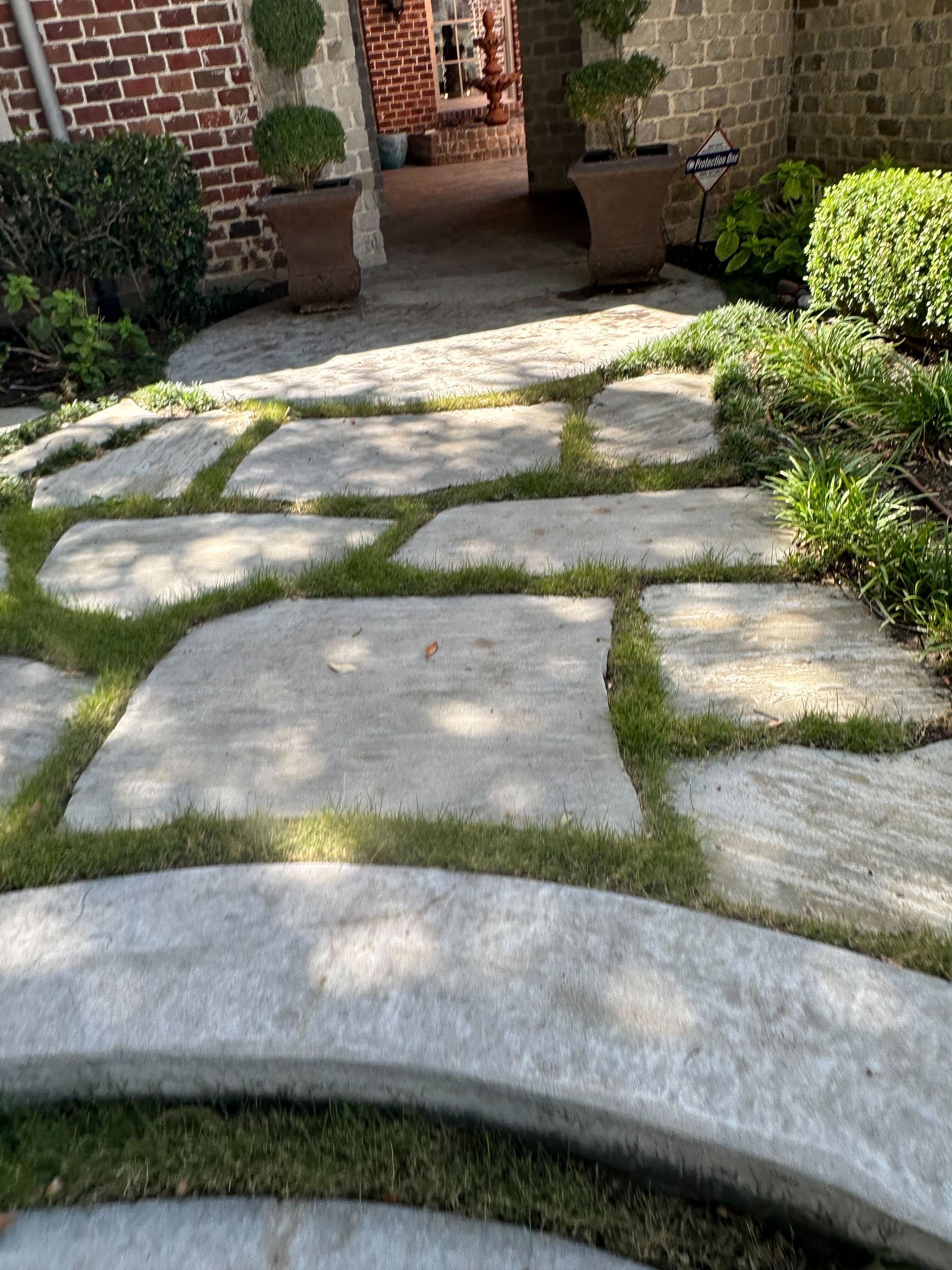 A stone walkway with grass growing on it in front of a brick building.