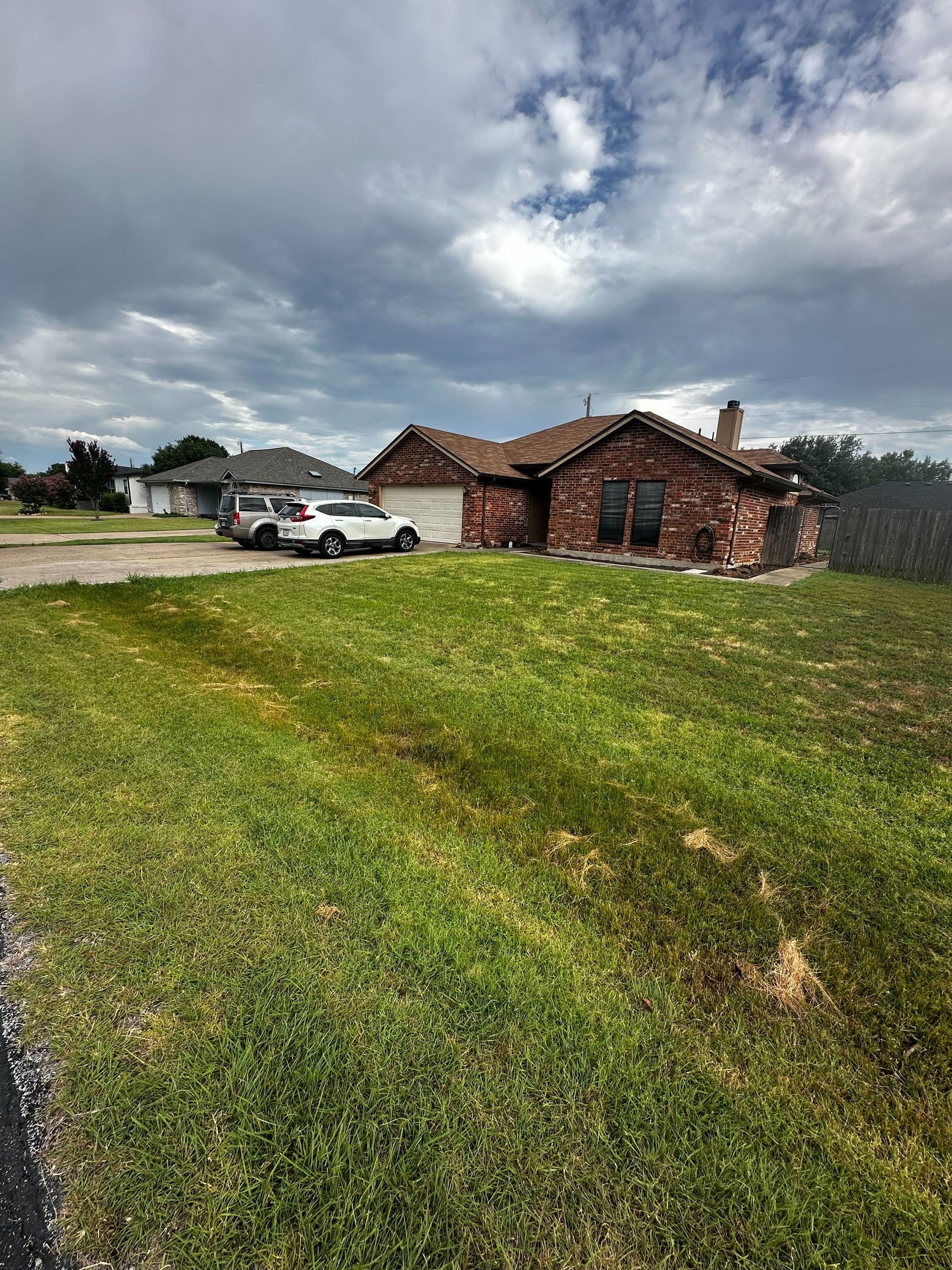 A white car is parked in front of a brick house.