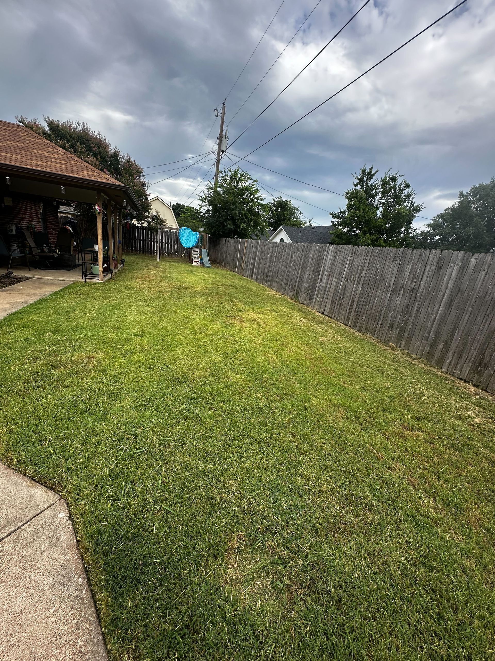 A lush green lawn with a wooden fence and a house in the background.