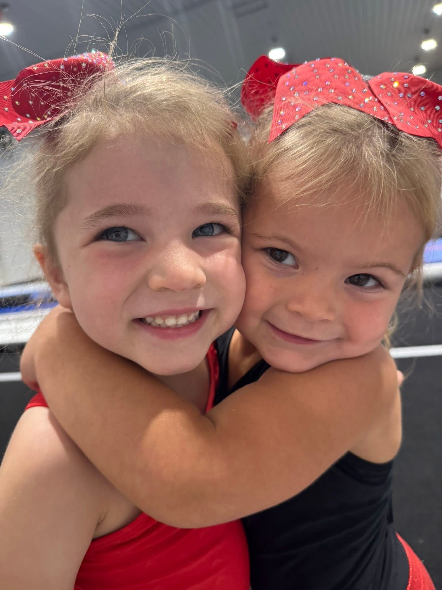 Four young children at a gymnastics gym: one doing a bridge pose, while the others watch and smile.