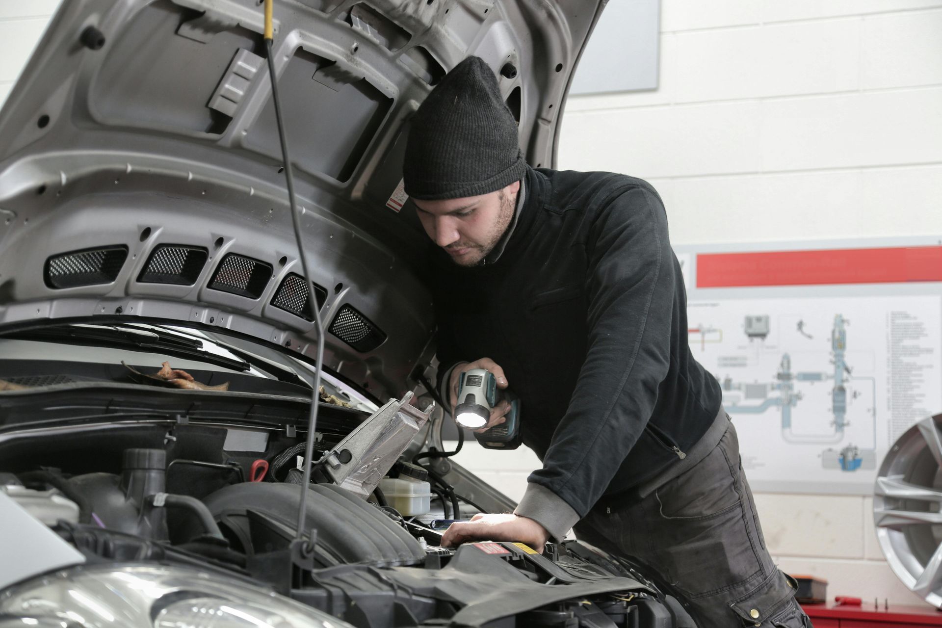 Mechanic inspecting a car engine with a flashlight in a garage.