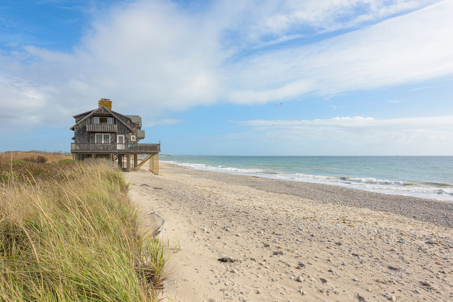 A house is sitting on top of a sandy beach next to the ocean.