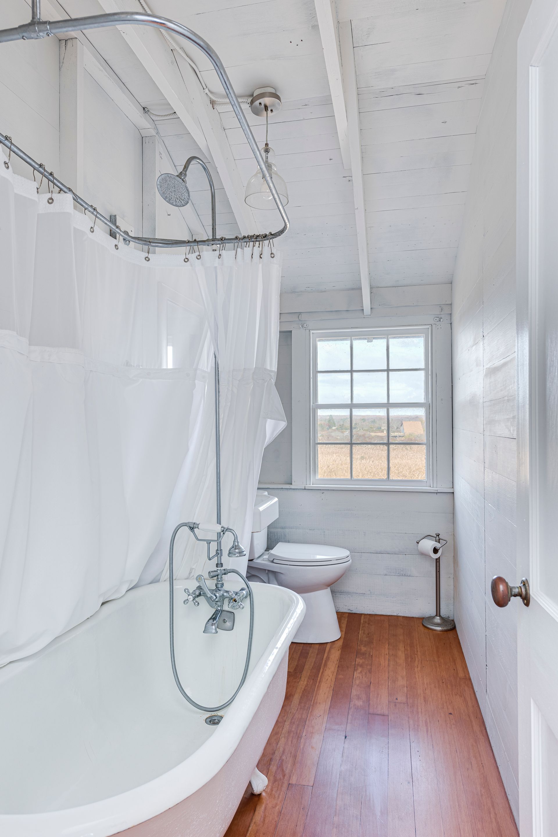 A bathroom with a tub , toilet , shower and window.