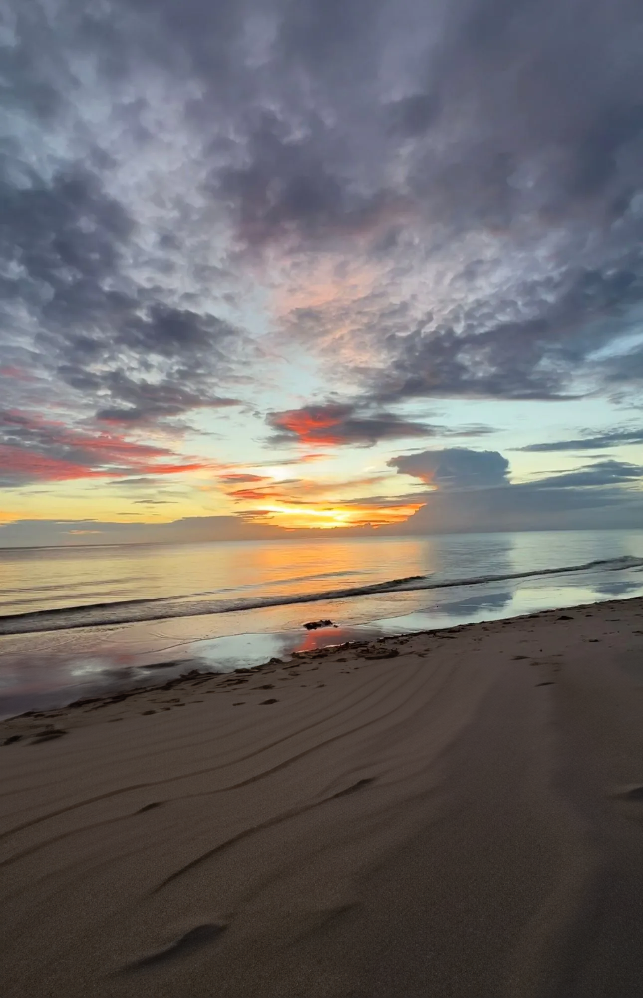 A sunset over a sandy beach with a cloudy sky