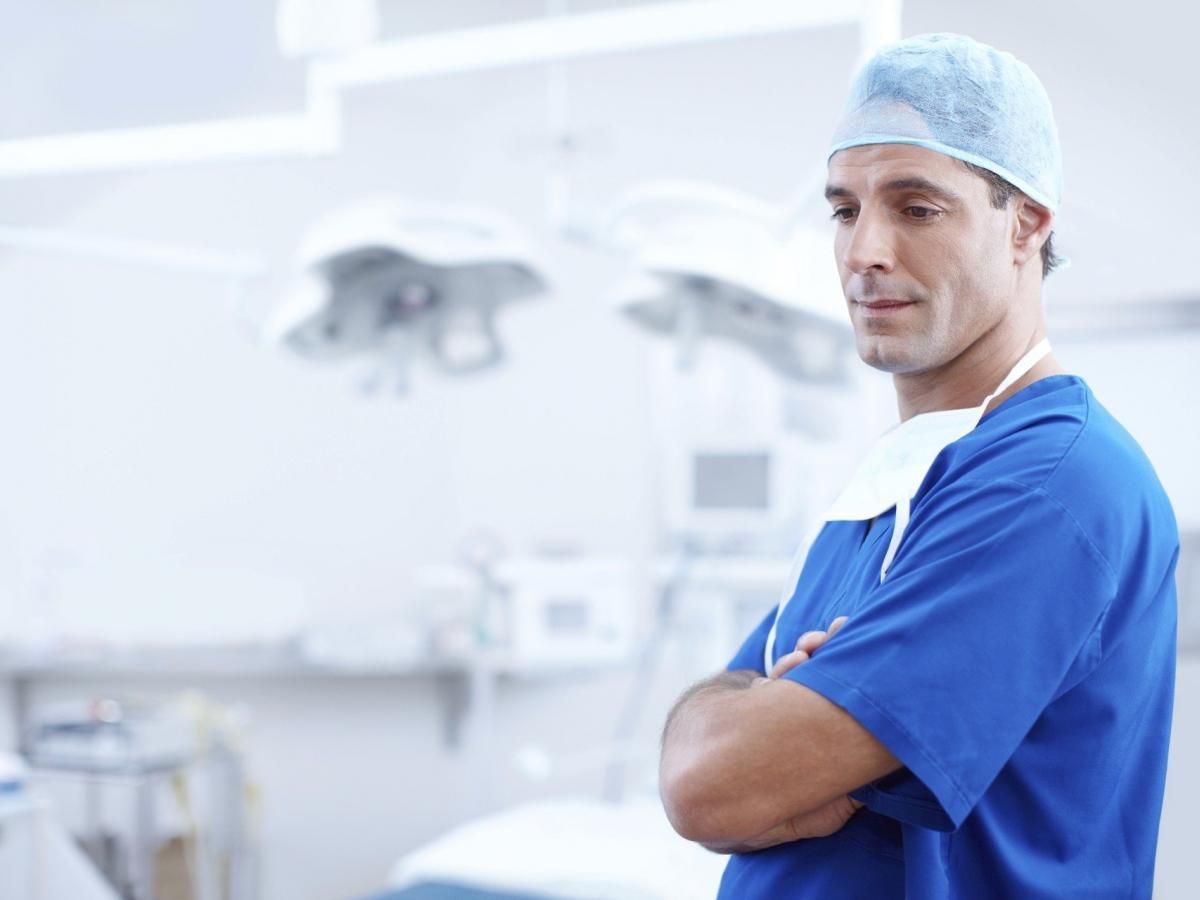 A surgeon is standing in an operating room with his arms crossed.