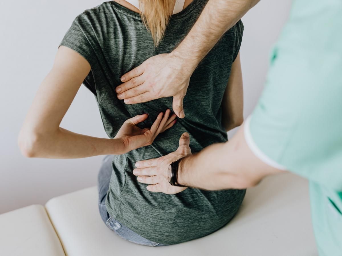 A woman is sitting on a table getting her back examined by a doctor.