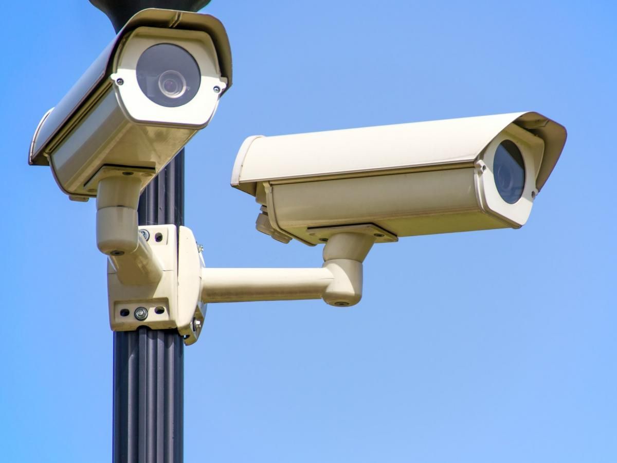 Two security cameras on a pole with a blue sky in the background