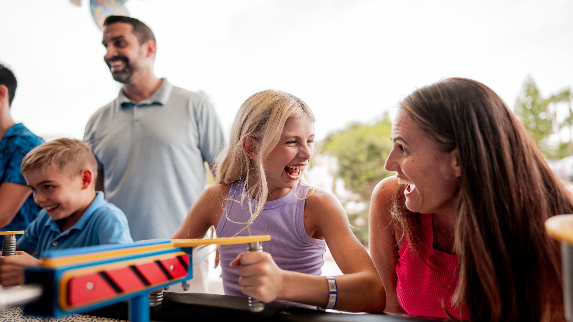 Family laughing while playing a game outdoors. Mother and daughter are in focus, holding handles of the game.