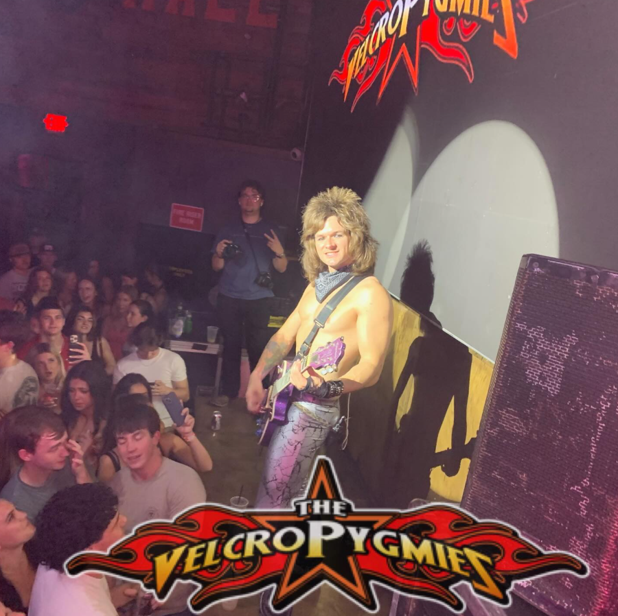 Singer onstage at a packed club, smiling under red lights, with the crowd pressed close below.