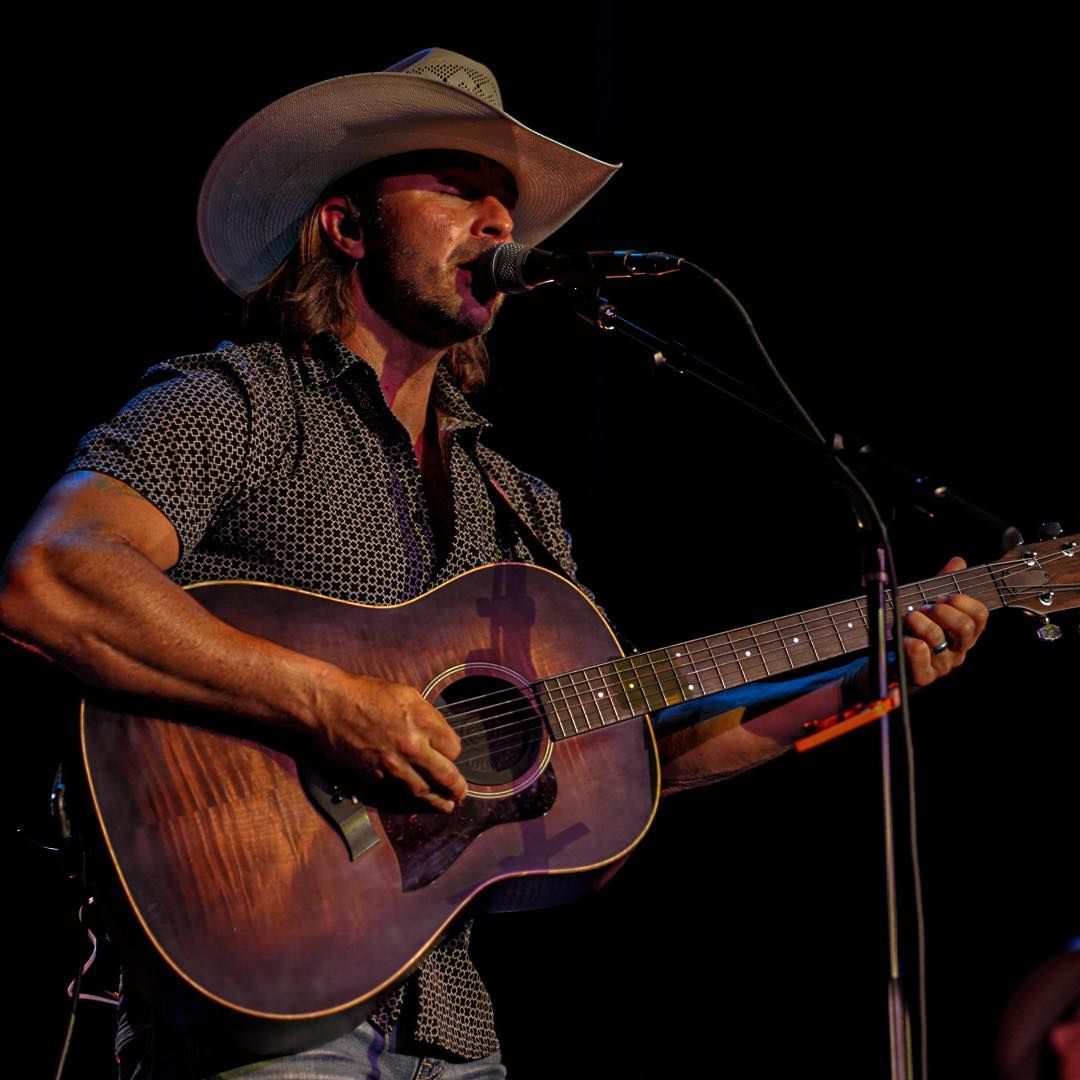 A man in a cowboy hat stands in front of a texas flag