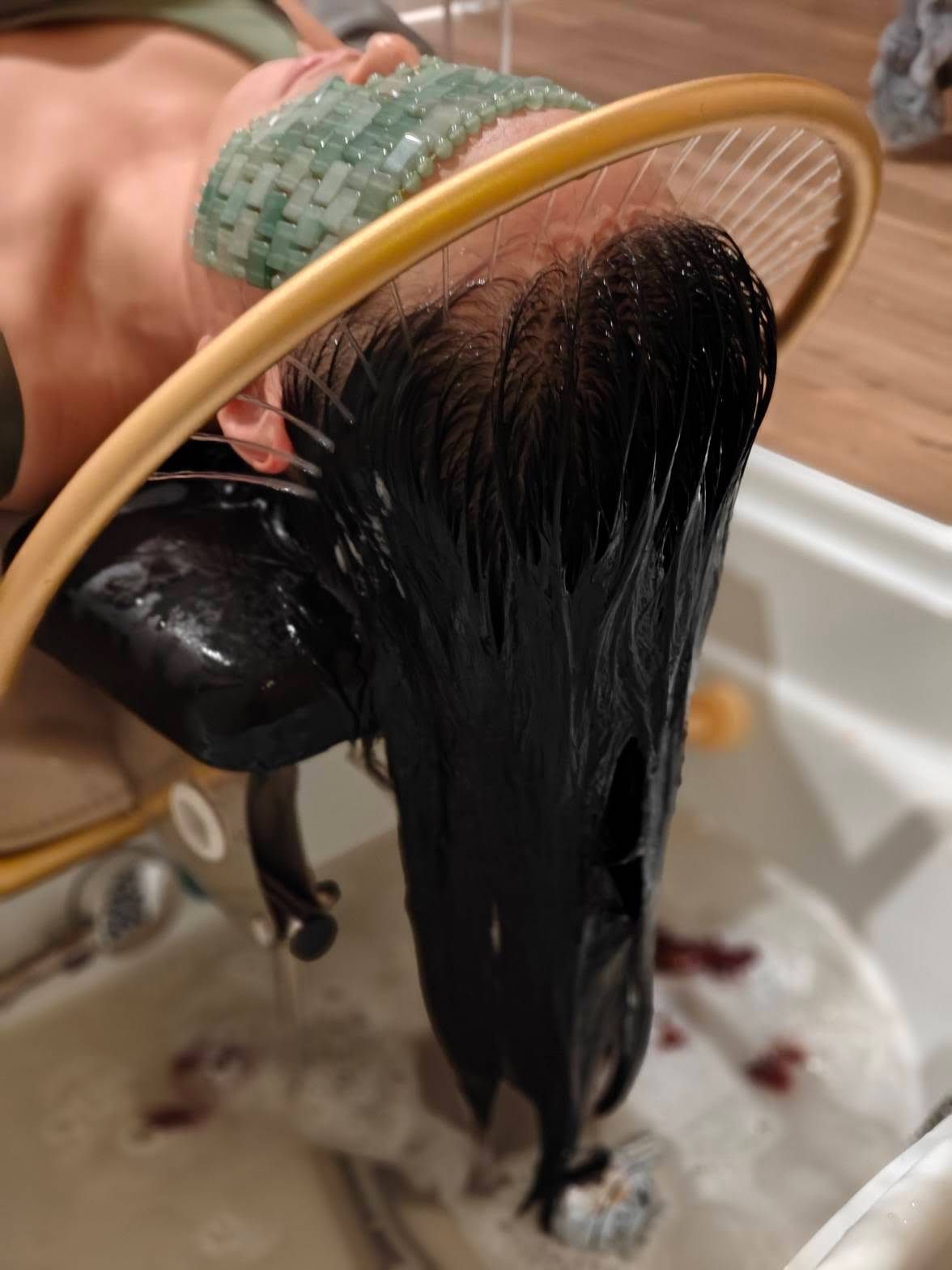 A woman is washing her hair in a sink with a hoop around her head.