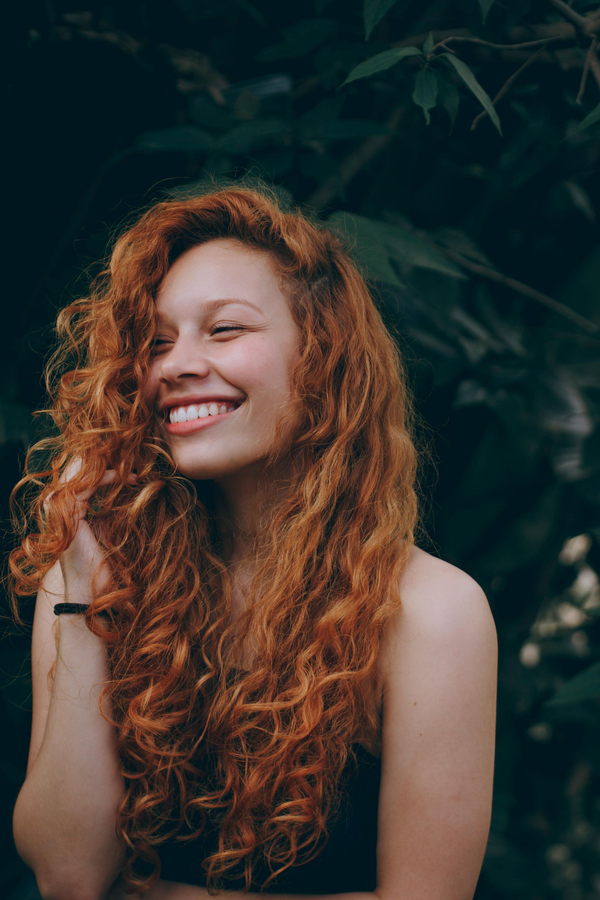 A woman with long red curly hair is smiling.