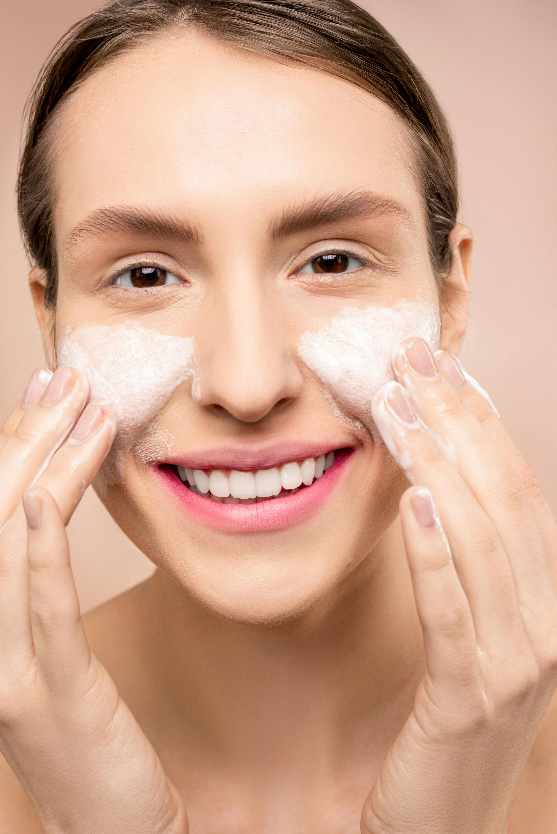 A woman is smiling while washing her face with soap.