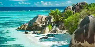 Tropical beach with turquoise water, white sand, large rocks, and green vegetation.